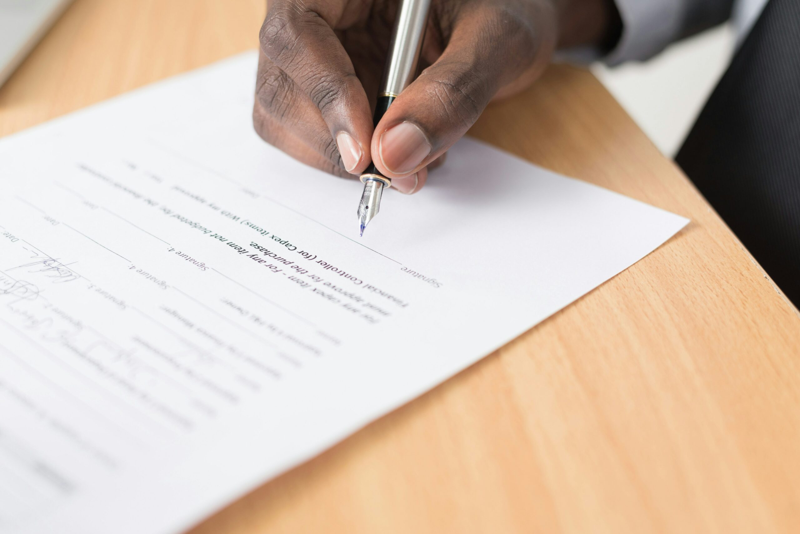 A person signing a document with a pen on a wooden desk.