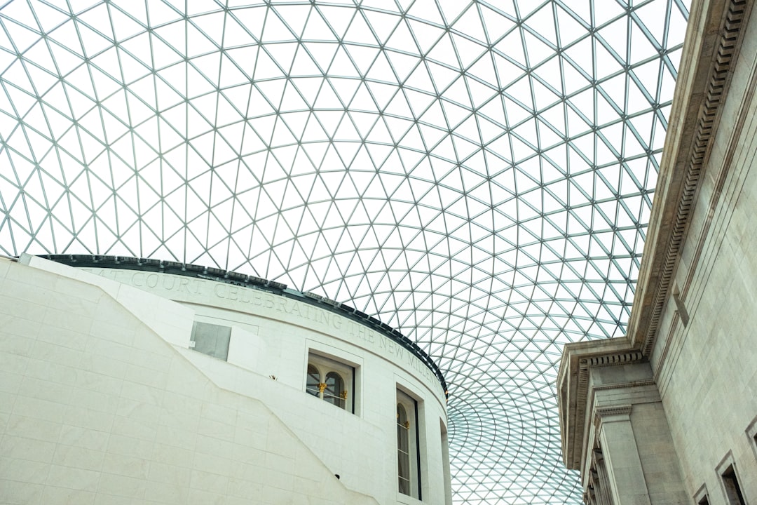 Glass and steel lattice ceiling over a white stone building structure inside a large atrium offers a striking visual interpretation, harmonizing modern design with historical perspective.