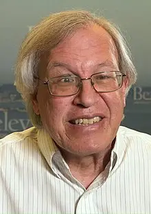 A smiling older man with glasses and gray hair in a striped shirt.