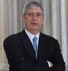 Man in a suit with crossed arms stands in front of large pillars.